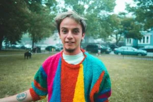 Myles Bullen smiles in a park, wearing a vibrant, multi-colored striped sweater.