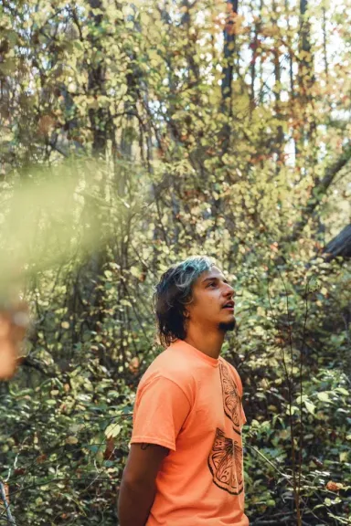 Myles Bullen looking up in a forest, wearing an orange t-shirt.
