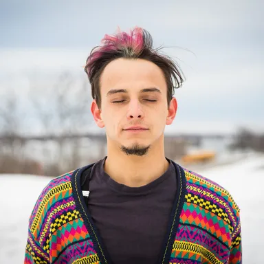Myles Bullen with eyes closed, wearing a colorful patterned cardigan in a snowy outdoor setting.