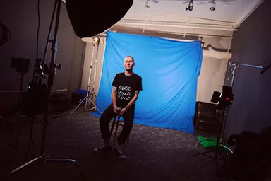 Factor Chandelier sitting on a stool in a studio with a blue backdrop and lighting equipment.